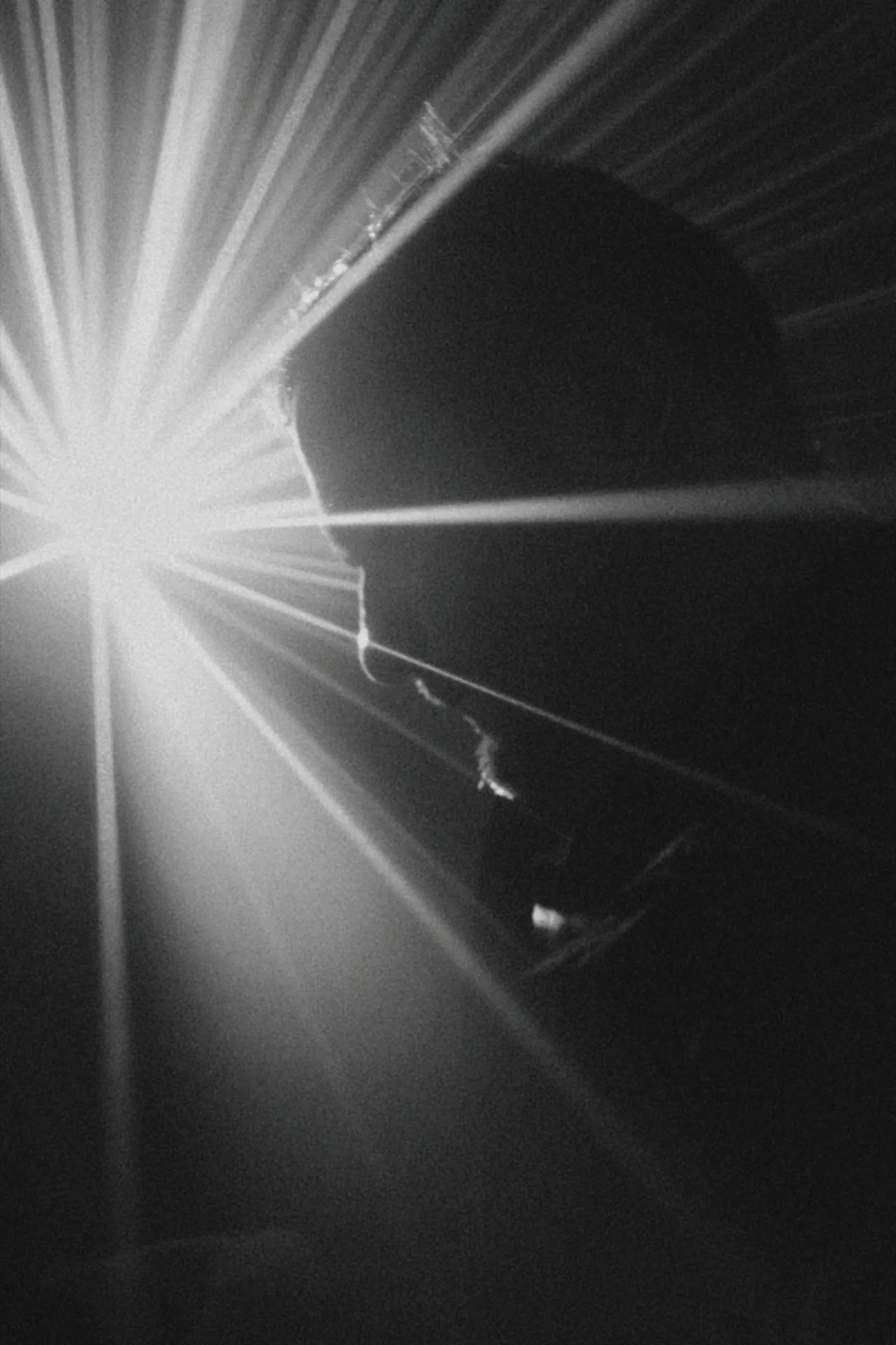 Nicholas Whitehead in silhouette, his head bowed, backlit by beams of stage light.